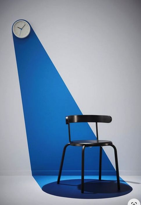 A black chair beneath a wall clock and a blue spotlight-shaped accent